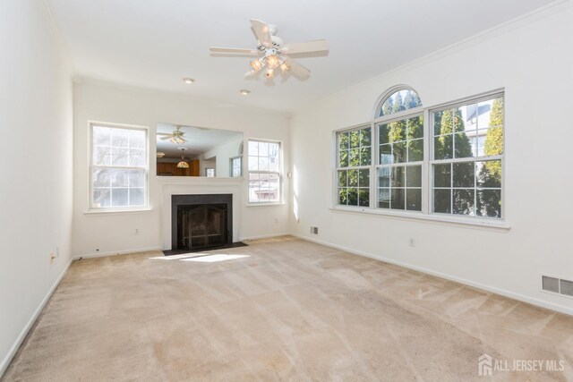unfurnished living room with crown molding, a fireplace with flush hearth, visible vents, ceiling fan, and carpet