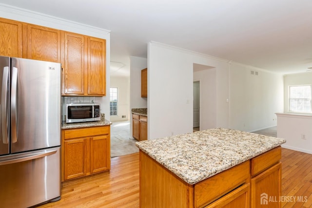 kitchen featuring light stone countertops, tasteful backsplash, light wood-type flooring, and appliances with stainless steel finishes