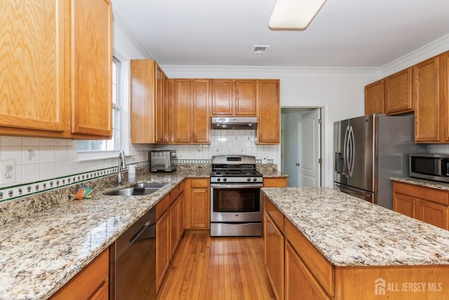 kitchen with a sink, crown molding, under cabinet range hood, and stainless steel appliances