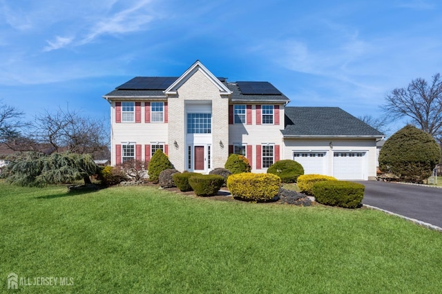 view of front of property featuring an attached garage, a shingled roof, a front lawn, aphalt driveway, and roof mounted solar panels