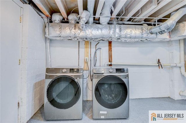 washroom featuring washing machine and clothes dryer and concrete block wall