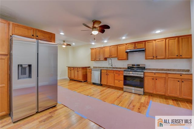 kitchen with stainless steel appliances, under cabinet range hood, light wood-style floors, ceiling fan, and a sink