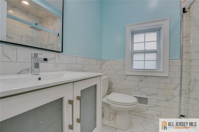 bathroom with tile walls, toilet, vanity, a tile shower, and wainscoting