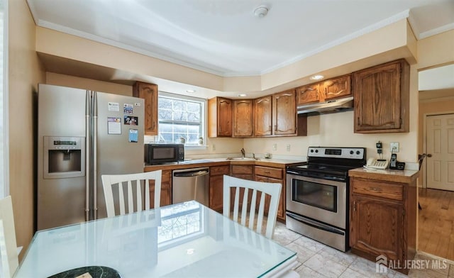 kitchen with appliances with stainless steel finishes, under cabinet range hood, ornamental molding, brown cabinetry, and light countertops