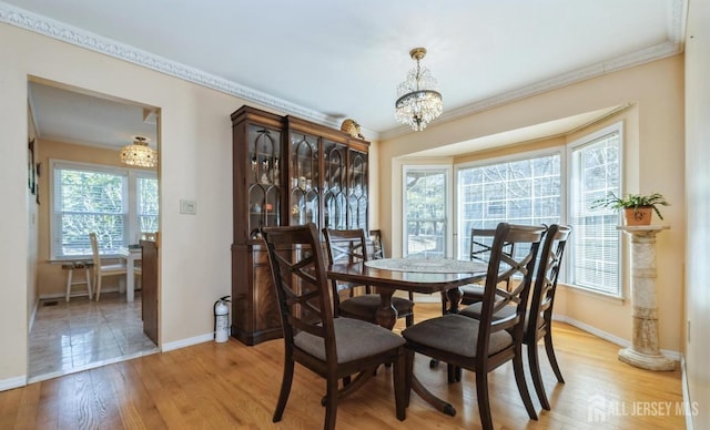dining area with baseboards, crown molding, a chandelier, and light wood finished floors