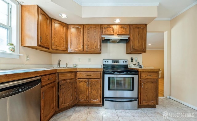 kitchen with appliances with stainless steel finishes, crown molding, brown cabinetry, light countertops, and recessed lighting