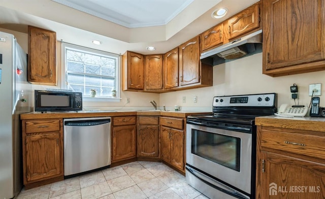 kitchen with appliances with stainless steel finishes, under cabinet range hood, crown molding, brown cabinetry, and light countertops