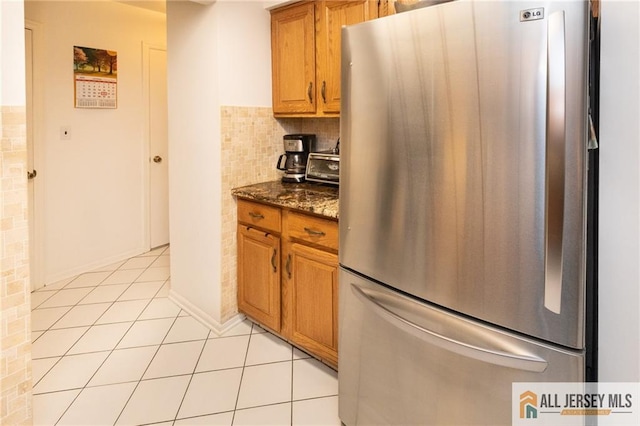 96 Riverbend Dr, North Brunswick, NJ 08902 - kitchen featuring freestanding refrigerator, light tile patterned flooring, dark stone countertops, brown cabinetry, and tasteful backsplash