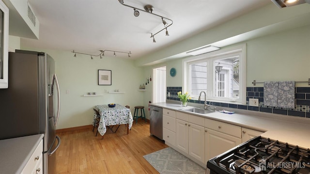 kitchen with light countertops, a sink, light wood-style floors, decorative backsplash, and appliances with stainless steel finishes