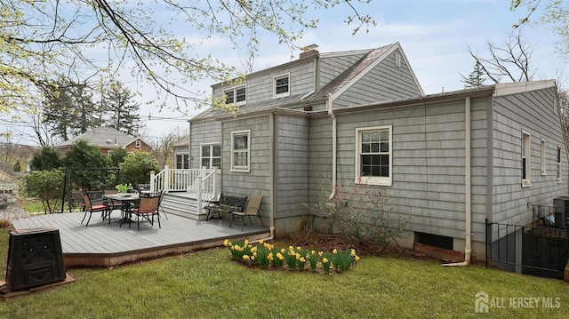rear view of property with a chimney, outdoor dining space, a yard, a wooden deck, and roof with shingles