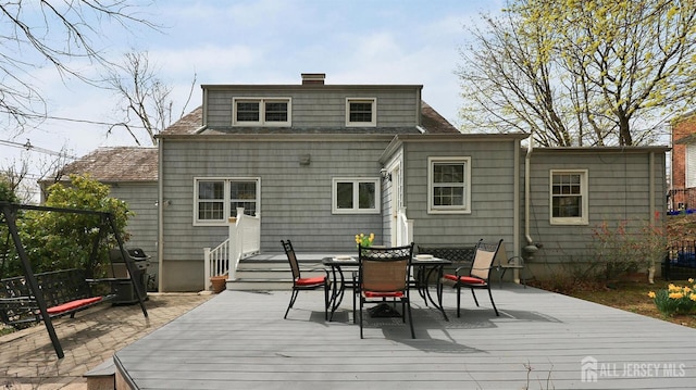 rear view of house with a wooden deck, outdoor dining space, a shingled roof, and a chimney