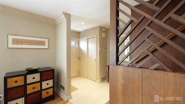 hallway with baseboards, ornamental molding, visible vents, and light tile patterned floors