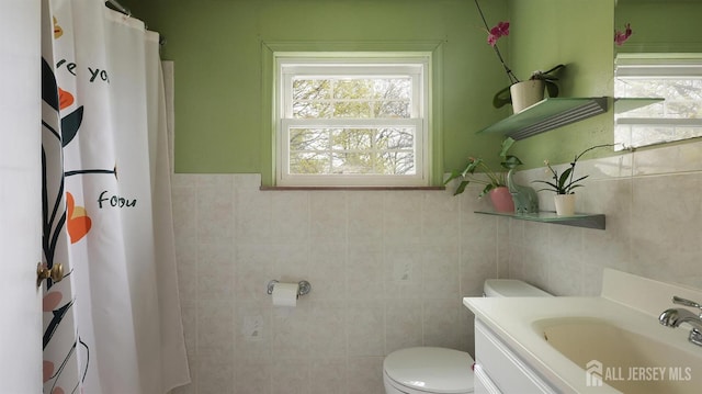 bathroom featuring wainscoting, toilet, vanity, and tile walls