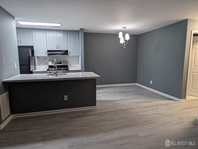 kitchen with light countertops, hanging light fixtures, freestanding refrigerator, a sink, and under cabinet range hood