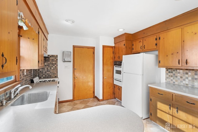 kitchen with a warming drawer, light countertops, decorative backsplash, a sink, and white appliances