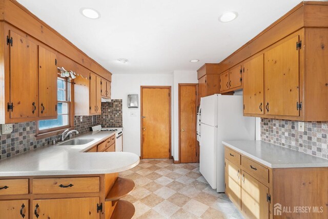 kitchen featuring kitchen peninsula, sink, stainless steel stove, tasteful backsplash, and white fridge