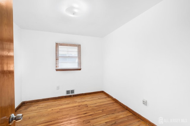 spare room with baseboards, visible vents, and wood finished floors