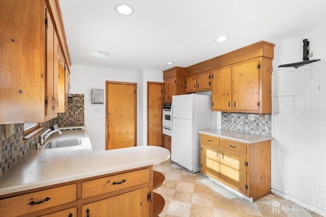 kitchen featuring recessed lighting, white appliances, a sink, light countertops, and tasteful backsplash