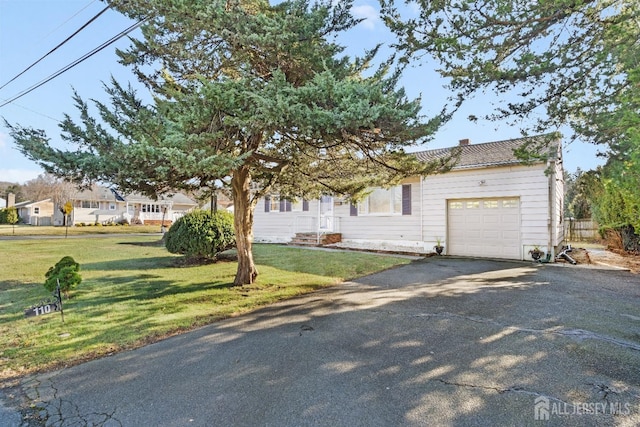 view of property hidden behind natural elements featuring a garage, a front lawn, and aphalt driveway