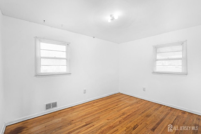 empty room with a wealth of natural light, wood finished floors, visible vents, and baseboards