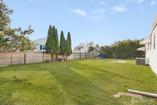 view of yard featuring a playground, a fenced backyard, and central AC unit