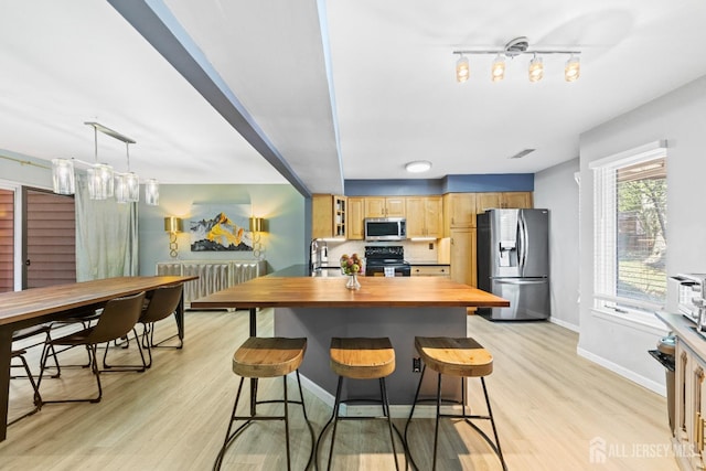 kitchen featuring light wood-style flooring, a sink, stainless steel appliances, a kitchen breakfast bar, and butcher block counters