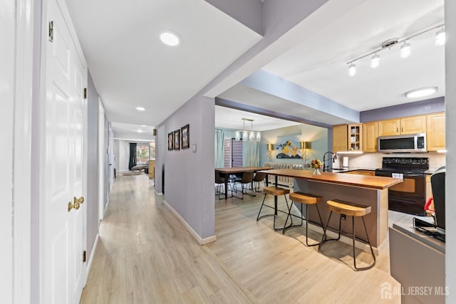 kitchen featuring a breakfast bar, light brown cabinetry, stainless steel microwave, black / electric stove, and wooden counters