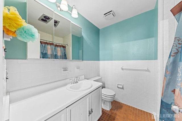 full bathroom featuring visible vents, tile walls, a wainscoted wall, toilet, and vanity