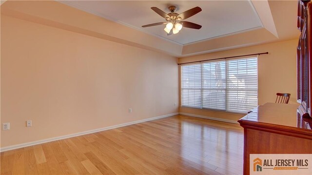 unfurnished office with ceiling fan, a tray ceiling, and light wood-type flooring