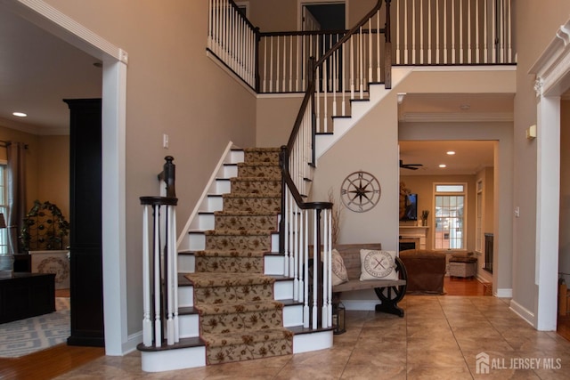 stairs with crown molding, a towering ceiling, tile patterned floors, and ceiling fan