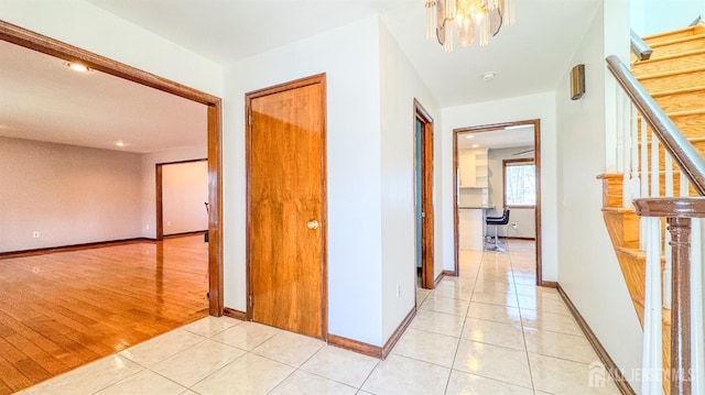 corridor featuring light tile patterned flooring, baseboards, stairway, and a notable chandelier