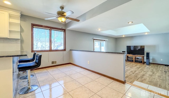 office with light tile patterned floors, baseboards, a skylight, visible vents, and a ceiling fan