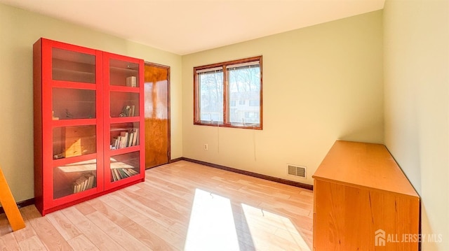 spare room with light wood-type flooring, visible vents, and baseboards