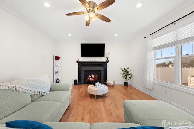 living area with baseboards, a glass covered fireplace, ornamental molding, light wood-type flooring, and recessed lighting