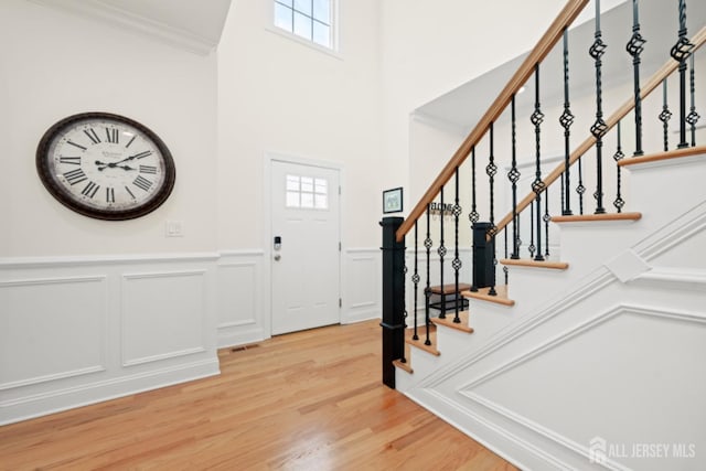 foyer with ornamental molding, light wood finished floors, wainscoting, and stairs