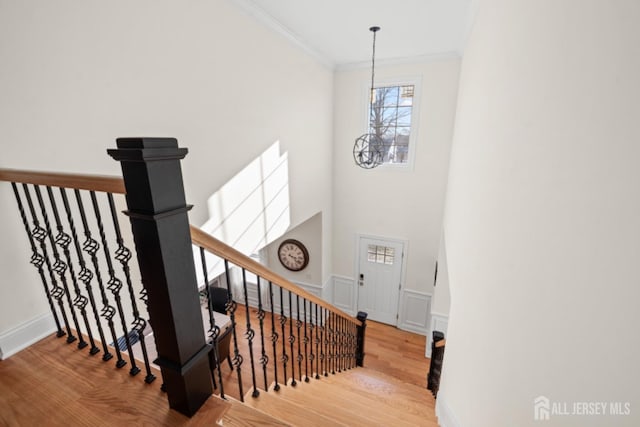 stairway featuring wainscoting, crown molding, an inviting chandelier, and wood finished floors