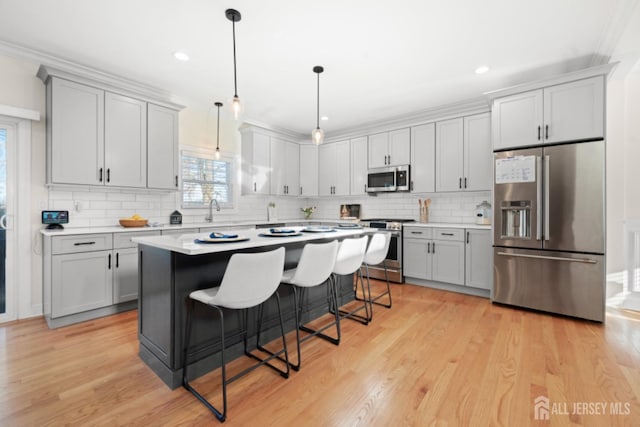 kitchen with stainless steel appliances, a breakfast bar, light countertops, light wood-type flooring, and gray cabinets