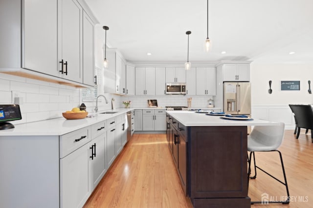 kitchen featuring a breakfast bar area, a center island, stainless steel appliances, light countertops, and a sink