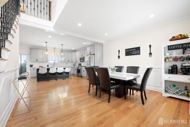 dining space featuring light wood finished floors, stairs, a decorative wall, and wainscoting