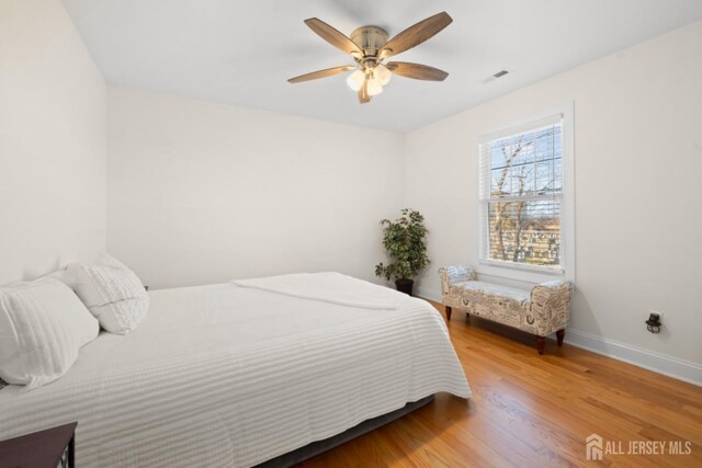 bedroom with a ceiling fan, wood finished floors, visible vents, and baseboards