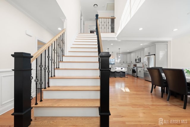 stairs featuring crown molding, recessed lighting, a decorative wall, wainscoting, and wood finished floors