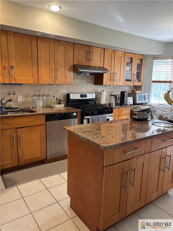 kitchen with under cabinet range hood, stainless steel appliances, brown cabinetry, and a sink