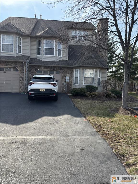 view of property featuring an attached garage, stone siding, driveway, and a chimney