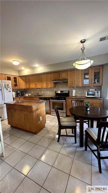 kitchen featuring stainless steel range with gas stovetop, brown cabinetry, freestanding refrigerator, and a center island