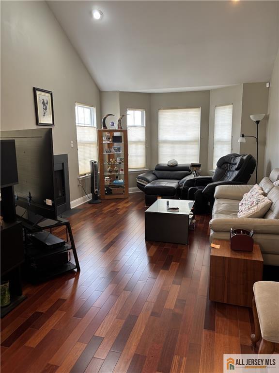 living area featuring dark wood-style floors, high vaulted ceiling, and baseboards