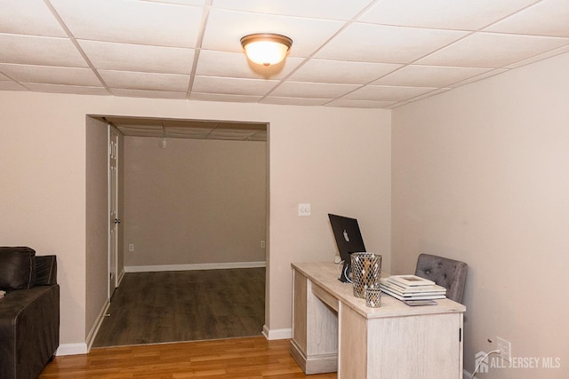 home office featuring light wood finished floors, a drop ceiling, and baseboards
