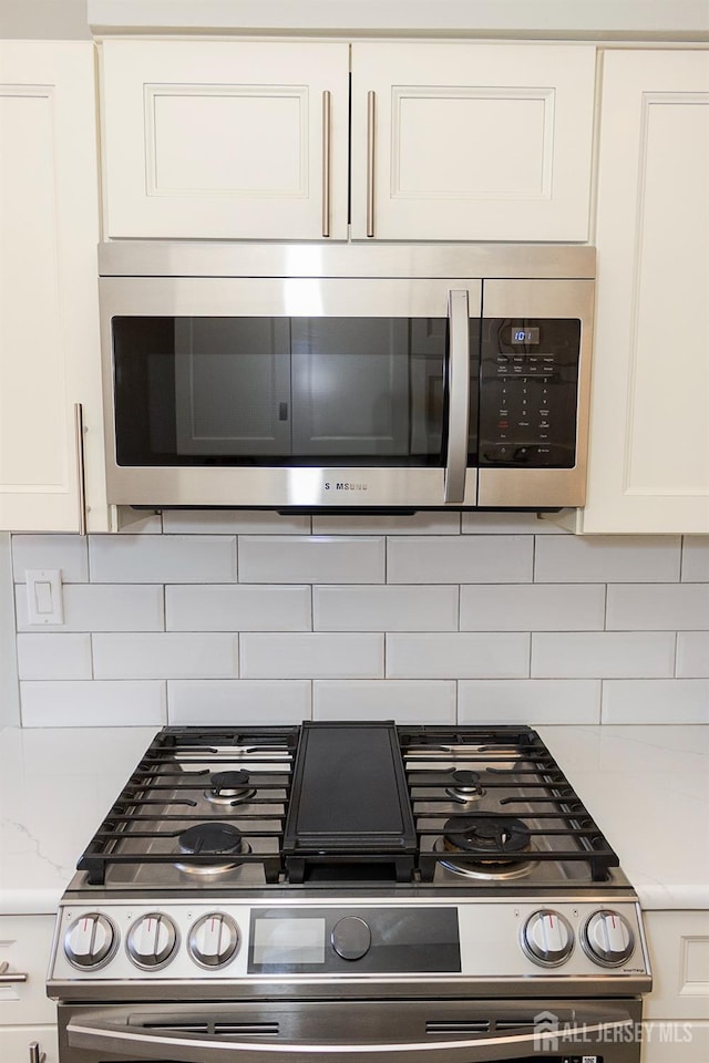 kitchen view of appliances with stainless steel finishes, white cabinetry, tasteful backsplash, and light stone counters