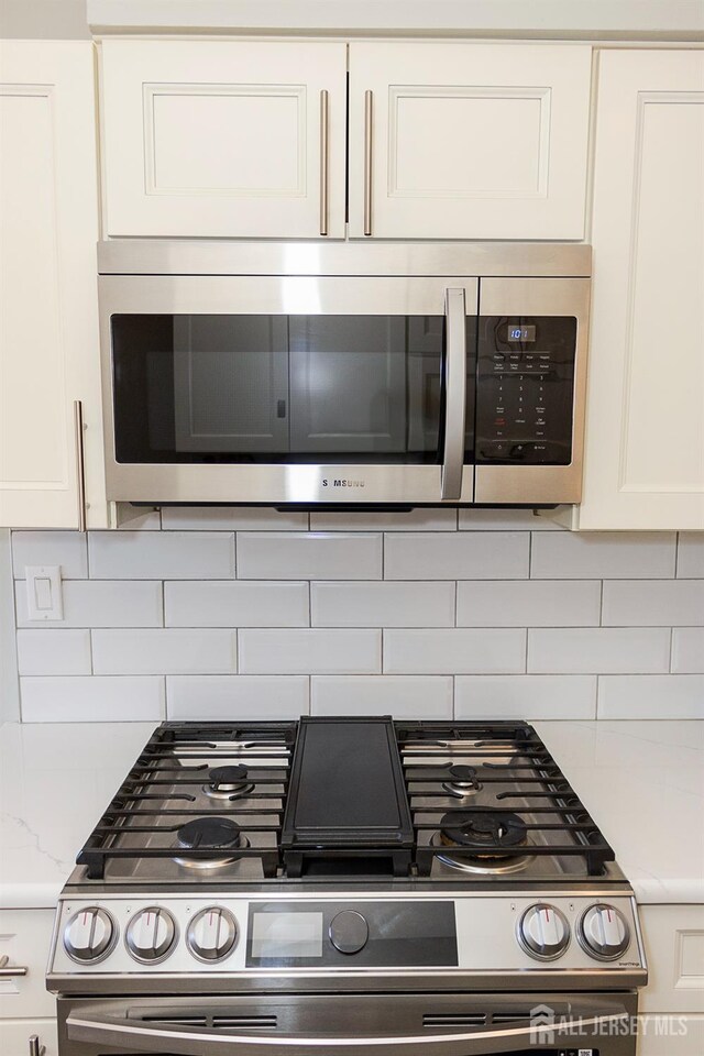 121 Sharon Garden Ct, Woodbridge Proper, NJ 07095 - kitchen view of appliances with stainless steel finishes, white cabinetry, decorative backsplash, and light stone counters