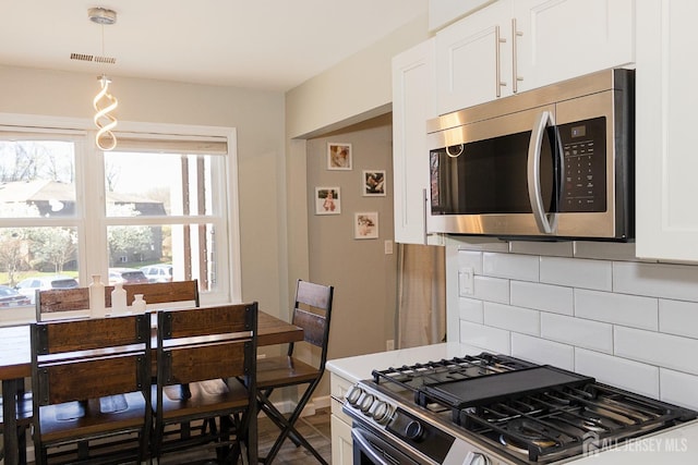 kitchen featuring stainless steel appliances, backsplash, white cabinets, and hanging light fixtures