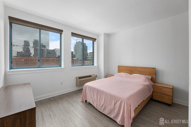 bedroom featuring wood finished floors, a city view, baseboards, and a wall mounted AC